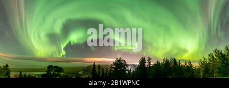 De magnifiques aurores boréales dans un ciel partiellement dégagé avec un épais brouillard se trouvent au-dessus du paysage forestier suédois en montagne, la ceinture verte de lumières nordiques est courbée Banque D'Images