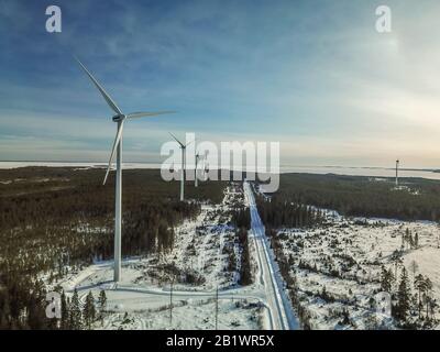 Belle photo aérienne de la ferme de moulin à vent et route droite en hiver forêt de pins, ciel bleu, mer ensoleillée, gelée à l'horizon, Suède Banque D'Images