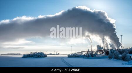Vue sur la centrale électrique de l'usine en hiver avec de la vapeur qui monte dans le ciel bleu profond, le port de mer avec le bateau, de nombreux réservoirs d'huile et deux moulins à vent à l'horizon Banque D'Images
