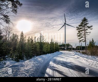 Photo de moulin à vent et route sinueuse en forêt de pins d'hiver, ciel bleu, brouillard d'hiver soleil, Suède, environnement écologique énergie verte Banque D'Images