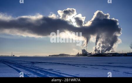 Vue de la centrale électrique de l'usine en hiver avec la vapeur qui s'élève dans un ciel bleu profond, le soleil brille derrière la vapeur, port maritime avec le bateau à l'horizon Banque D'Images