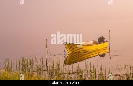 Un petit bateau à moteur, beau soleil doré brille par un épais brouillard au lac pendant le lever du soleil tôt, l'eau calme Banque D'Images