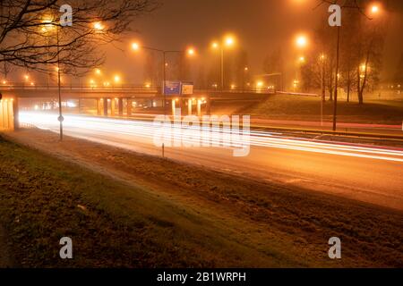 Des traces lumineuses colorées et floues de la circulation nocturne sur l'autoroute de la ville d'Umea, un temps d'automne brumeux, en Suède Banque D'Images