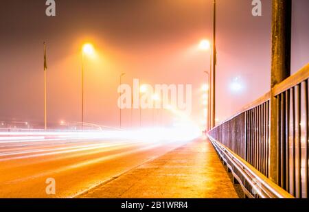 Des traces de lumière colorées de la circulation nocturne animée sur le pont central de la ville d'Umea, vue du côté droit, brouillard météo d'automne, Suède Banque D'Images
