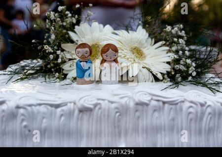 Figurines sur un gâteau de mariage avec bouquet de fleurs au coucher du soleil avec la fête hors du foyer en arrière-plan Banque D'Images