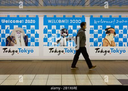 Un Japonais, portant un masque facial en papier, passe devant des affiches accueillant des gens à Tokyo pour les Jeux olympiques de 2020. Gare de Shinjuku, Tokyo, Japon, Banque D'Images