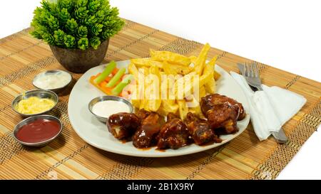 Plaque blanche avec ailes de poulet barbecue accompagnées de frites, de carottes et de céleri, avec sauces dans de petites assiettes sur fond blanc Banque D'Images