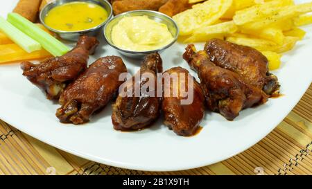 Plaque blanche avec ailes de poulet barbecue accompagnées de frites, de carottes et de céleri, avec sauces dans de petites assiettes sur fond blanc Banque D'Images