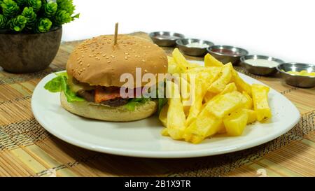 Plaque blanche avec hamburger à la viande, bacon et laitue accompagnés de frites et de sauces dans de petites assiettes sur fond blanc Banque D'Images