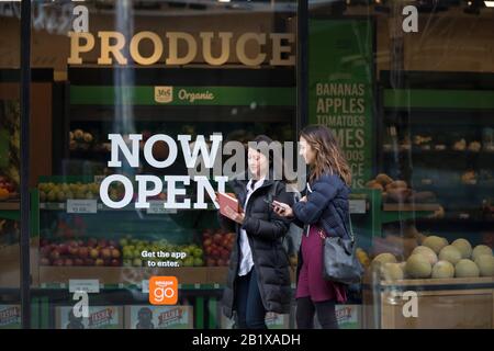 Deux jeunes femmes marchent le long de Pike Street devant la boutique Amazon Go Grocery le 27 février 2020. Le premier supermarché sans cashierless de la société de technologie a ouvert ses portes dans le quartier Capitol Hill de Seattle plus tôt dans la semaine. Les clients numérisent une application Amazon Go pour entrer dans la boutique de 10 000 pieds carrés, emporter les produits et aller sans quitter. La « technologie De Sortie Simple » d'Amazon utilise un système complexe de caméras et de capteurs pour suivre les achats est déjà utilisée dans leurs petits magasins Amazon Go. Banque D'Images