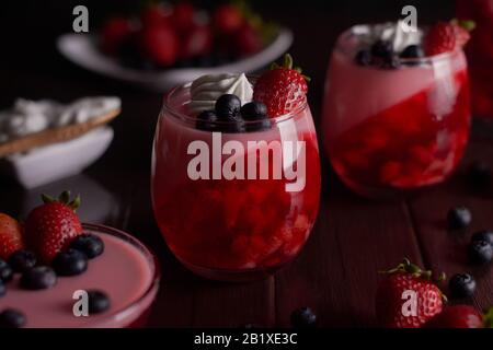 Desserts à base de gelée de fruits rouges crème chantilly et bleuets et fraises en verre sur fond brun en bois Banque D'Images