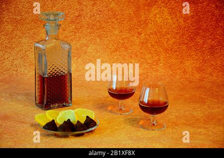 Décanteur de cristal avec cognac et deux verres de boisson à côté d'une assiette avec hors-d'œuvre, couper les bonbons au citron et au chocolat. Gros plan. Banque D'Images