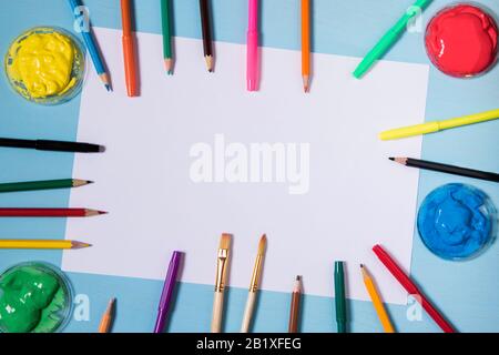 Feuille de papier blanche sur un fond bleu avec espace de copie et de place pour inscrire une couleur autour des peintres et des pinceaux d'encre de plume et des crayons copie également spac Banque D'Images