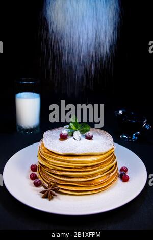 Délicieux crêpes sur une plaque blanche avec des poudings aux canneberges et de la cannelle saupoudrés de sucre en poudre, de confiture de bleuets et d'un verre de vert au lait Banque D'Images