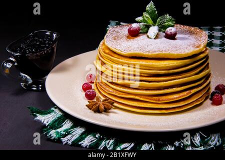 Délicieux crêpes sur une plaque blanche avec des lingettes vertes, des poudings aux canneberges et de la cannelle saupoudrés de sucre avec de la confiture de bleuets et un verre Banque D'Images