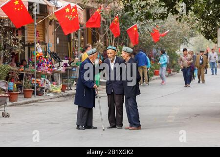 Trois hommes âgés de la minorité Uyghur ayant une conversation dans une rue de la vieille ville de Kashgar. Des drapeaux chinois sont montés sur la maison à l'arrière. Banque D'Images