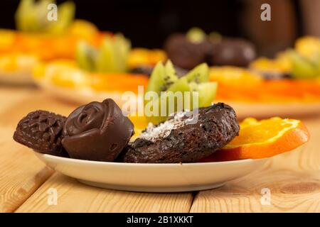 Des bonbons au chocolat et des biscuits saupoudrés de flocons de coco se trouvent avec des fruits hachés sur une soucoupe blanche sur une table en bois. Cuisson maison avec la santé Banque D'Images