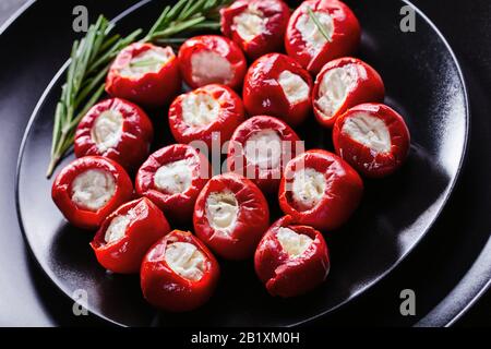 Poivrons de cerise marinés farcis au fromage ricotta doux servis sur une plaque noire avec des brins de romarin sur un fond en béton foncé, orienta horizontal Banque D'Images