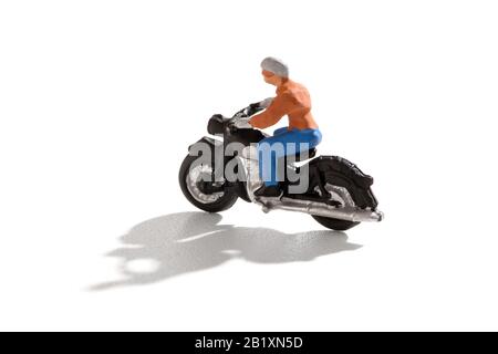 Personne miniature qui monte une moto avec ombre sur un fond blanc en vue latérale et espace de copie Banque D'Images