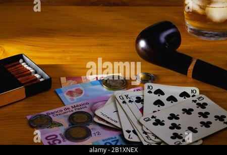 Jeux de hasard - pipe à fumer, cartes à jouer, whisky écossais et billets de banque au mexique sur la table en bois Banque D'Images