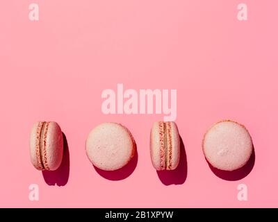 Macarons roses avec espace de copie. Rangée de macarons ou macarons français parfaits sur fond rose. Vue de dessus ou plat. Lumière dure Banque D'Images