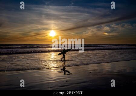 Surfez sur la plage en face du coucher du soleil à la Costa de la Luz, Andalousie, Espagne. Banque D'Images