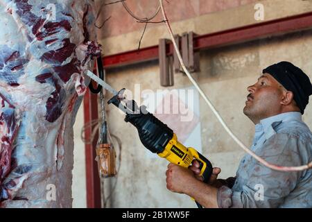 Ankara/Turquie-août 08 2019: Boucher mâle à l'aide d'une tronçonneuse pour couper la viande suspendue dans un abattoir. Banque D'Images