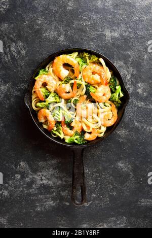 Gros plan de crevettes et de pâtes de brocoli dans une poêle en fonte sur fond de pierre sombre. Délicieux plat sain pour le dîner. Vue sur le dessus, plat Banque D'Images