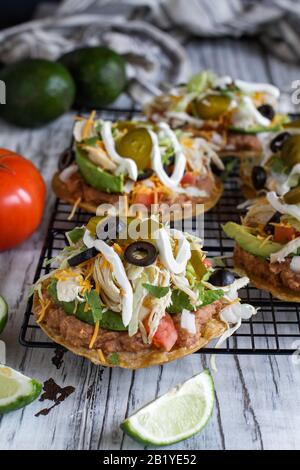 Tostadas faits maison au poulet avec haricots pinto frits, cilantro frais, fromage cheddar râpé, avocats, olives noires, crème aigre, laitue, jalapenos, l Banque D'Images