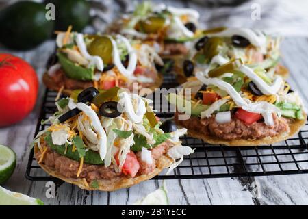 Tostadas faits maison au poulet avec haricots pinto frits, cilantro frais, fromage cheddar râpé, avocats, olives noires, crème aigre, laitue, jalapenos, l Banque D'Images