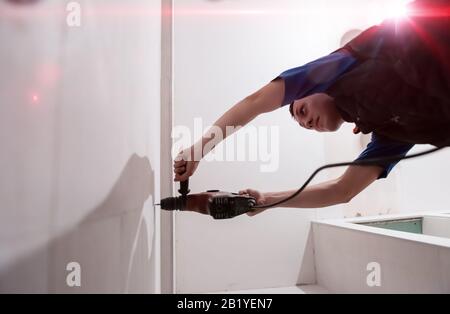 jeune travailleur de la construction forer des trous dans le mur de la salle de bains pour installer des accessoires de salle de bains Banque D'Images