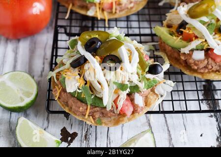 Tostadas faits maison au poulet avec haricots pinto frits, cilantro frais, fromage cheddar râpé, avocats, olives noires, crème aigre, laitue, jalapenos, l Banque D'Images