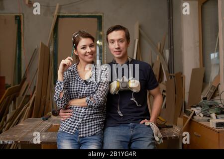 Jeunes couples de menuisiers assis en atelier sur fond de planches Banque D'Images