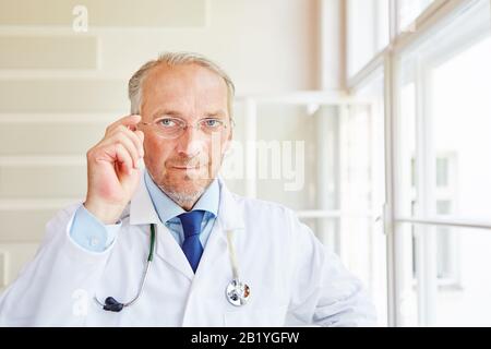 Homme senior en tant que médecin dans un manteau blanc dans sa pratique Banque D'Images