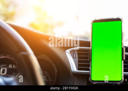 Un gadget moderne pour smartphone est monté sur le support du téléphone sur le tableau de bord de la voiture. Modèle isolé de l'écran à touches chroma vert maquette. CopySpace pour le texte Banque D'Images