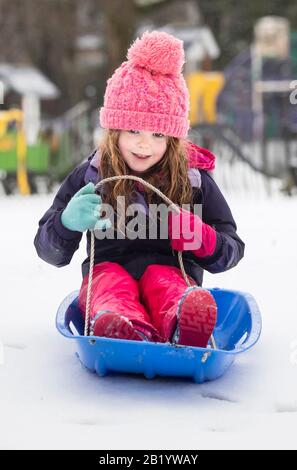 EMMIE Fielden, 5 ans, joue sur ses conditions de neige en traîneau dans les jardins du Pavillon, Buxton, Derbyshire, alors que de la neige frappe le Royaume-Uni. Banque D'Images