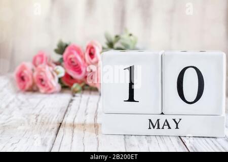 Blocs calendrier en bois blanc avec la date du 10 mai pour la fête des mères. Foyer sélectif avec ranunculus rose en arrière-plan sur une table en bois. Banque D'Images