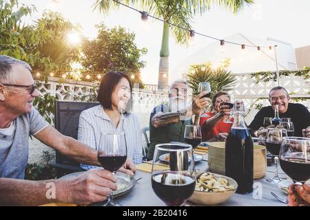 Bonne famille manger et boire du vin rouge au dîner barbecue en plein air - des amis fatigués se dégustant ensemble au restaurant Banque D'Images