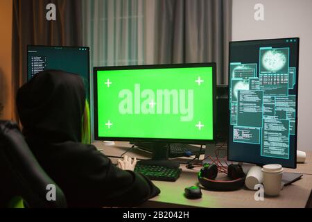 Dangereux hacker à capuchon femelle devant l'ordinateur avec écran vert. Banque D'Images