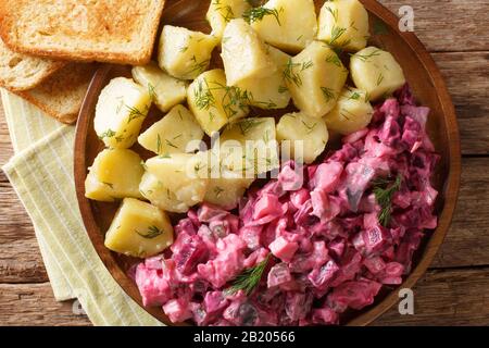 salade de hareng avec betteraves, oignons, pommes, marinés avec un plat latéral de pommes de terre bouillies dans une assiette sur la table. Vue de dessus horizontale Banque D'Images