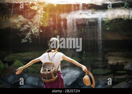 Jeune femme assise devant la cascade avec lever les bras Banque D'Images