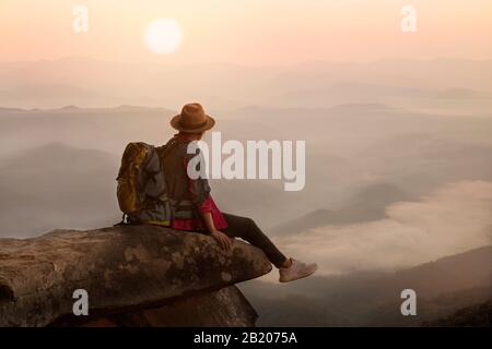 Backpacker homme assis sur la falaise avec le coucher de soleil arrière-plan Banque D'Images