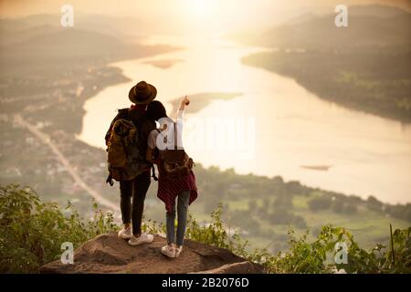 couple backpacker debout sur la falaise avec le coucher de soleil arrière-plan Banque D'Images