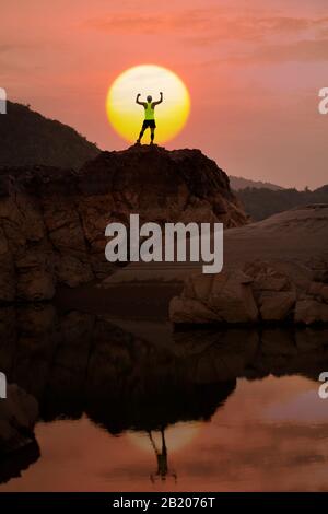 sportif debout au sommet de la montagne, levant les mains avec coucher du soleil ou fond de lever de soleil Banque D'Images