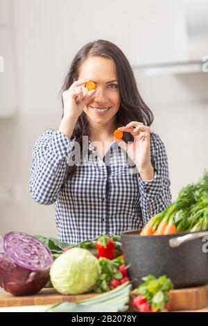 Jeune femme espiègle tenant des tranches de carotte dans la cuisine - régime de légumes et de la santé concept. Banque D'Images