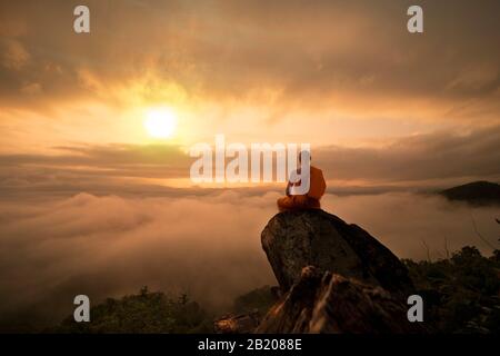 Le moine bouddhiste en méditation dans le magnifique coucher du soleil ou le lever du soleil sur la haute montagne d'arrière-plan Banque D'Images