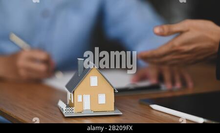 La photo courte de l'agent Immobilier offre l'assurance maison ou la propriété de maison à l'homme intelligent en chemise bleue à la table en bois moderne. Signature de l'accord Banque D'Images