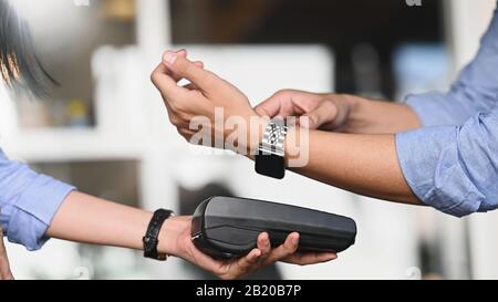 Image rognée D'Un Homme D'Affaires faisant un paiement en utilisant une montre intelligente avec café / restaurant flou comme arrière-plan. Concept de technologie NFC. Banque D'Images