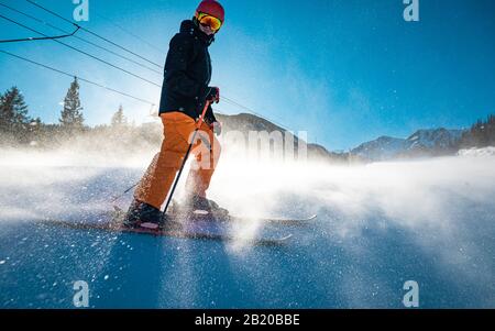 Skier sur une pente debout encore pendant que la neige vole autour de ses jambes et skis Banque D'Images