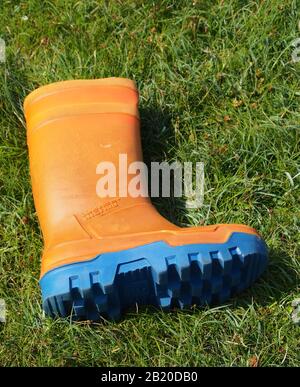 Une chaussure wellington orange de pêcheur avec une bande de roulement bleue qui s'est posée sur l'herbe Banque D'Images